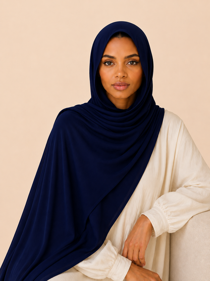 Elegant woman wearing a deep navy modal hijab with soft luxurious drape looking directly at the camera in a clean neutral studio setting