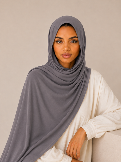 Elegant woman wearing a taupe grey bamboo modal hijab with soft luxurious drape in a clean beige studio setting looking directly at the camera